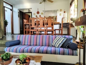 Ein Wohnzimmer mit einem gestreiften Sofa, einem Couchtisch mit Pflanzen und einem Essbereich mit Holzsesseln und einem Tisch.