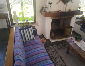 A cozy living room with a striped sofa, a fireplace, and a view of greenery outside. - Complete property with access to the reservoir, pets allowed. (Atibaia)