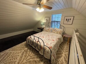 Ein Schlafzimmer mit einem Bett, einem Deckenventilator, einem Fenster und einer Heizung.