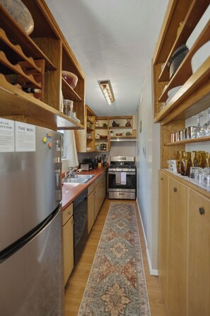 Eine kleine Küche mit Holzschränken, einem Edelstahlkühlschrank, einem Herd und einem Spülbecken.