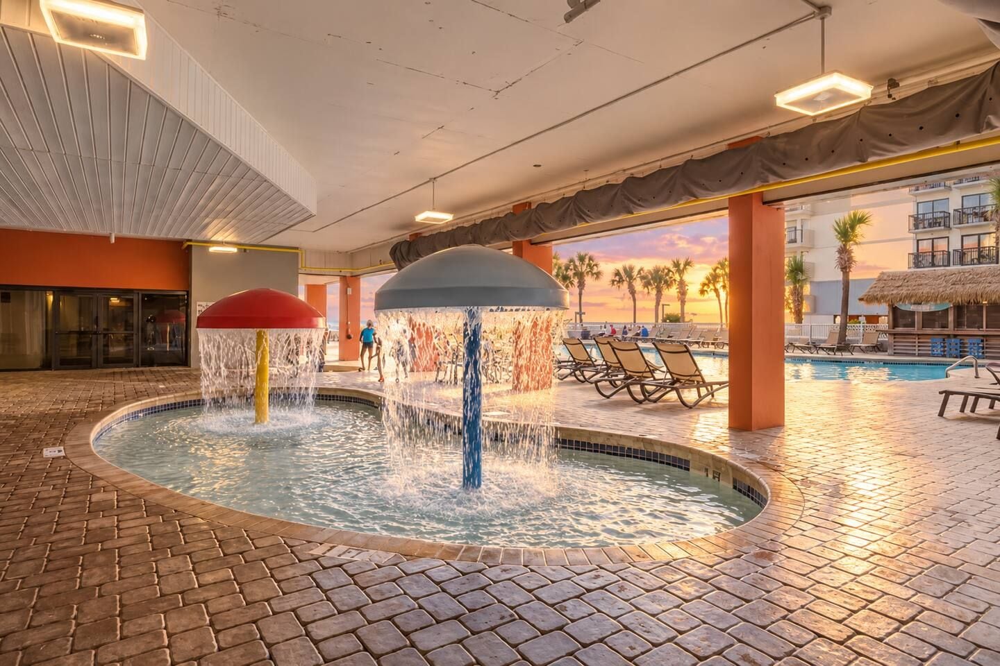 An indoor swimming pool with water features, lounge chairs, and a view of the outside.