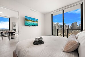 Ein Hotelzimmer mit großem Bett, Blick auf die Stadt, Essbereich mit Tisch und Stühlen sowie Fernseher an der Wand.