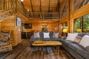 A wooden cabin interior with a sofa, dining table, and a staircase. - Riverfront A-Frame | Hot Tub + Fireplace (Ellijay)