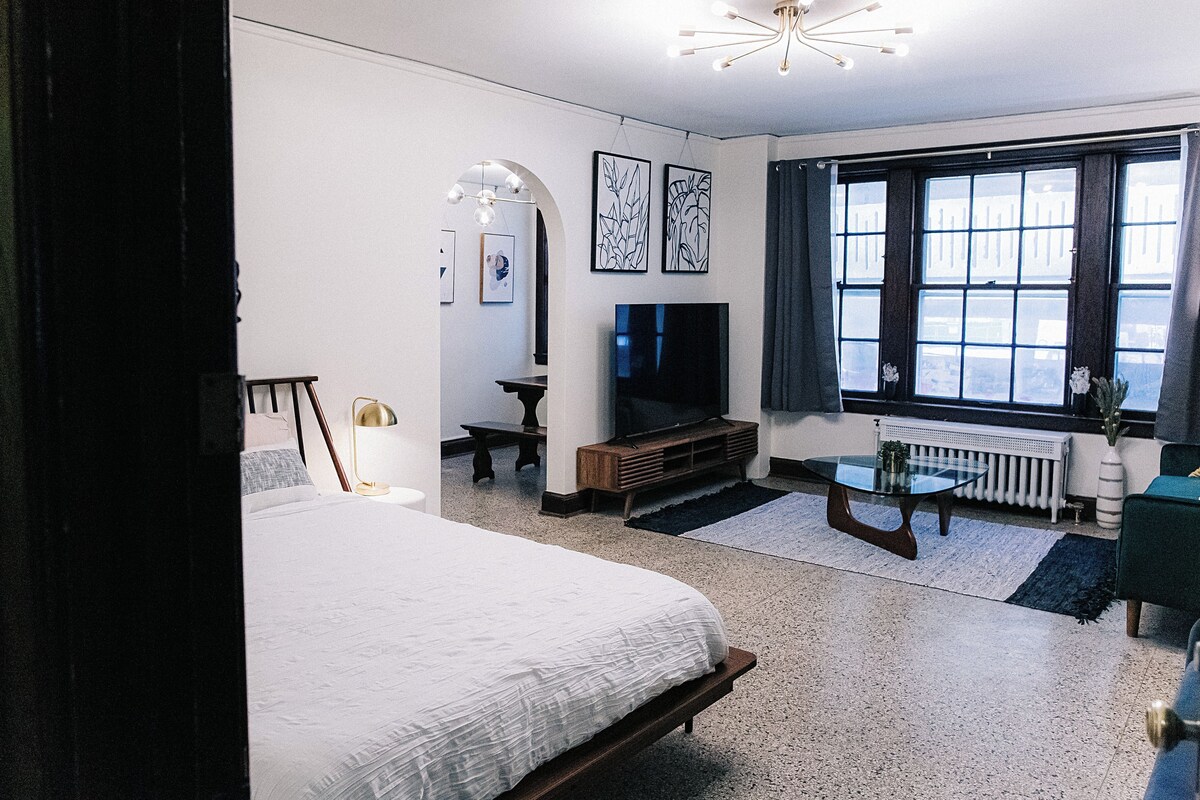 A modern bedroom with a bed, a TV, a small table, and artwork on the wall.