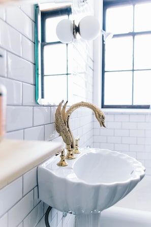A bathroom with a white sink, a gold faucet, and a window with a view. - The Wilson by Voyageur Stays (Madison)