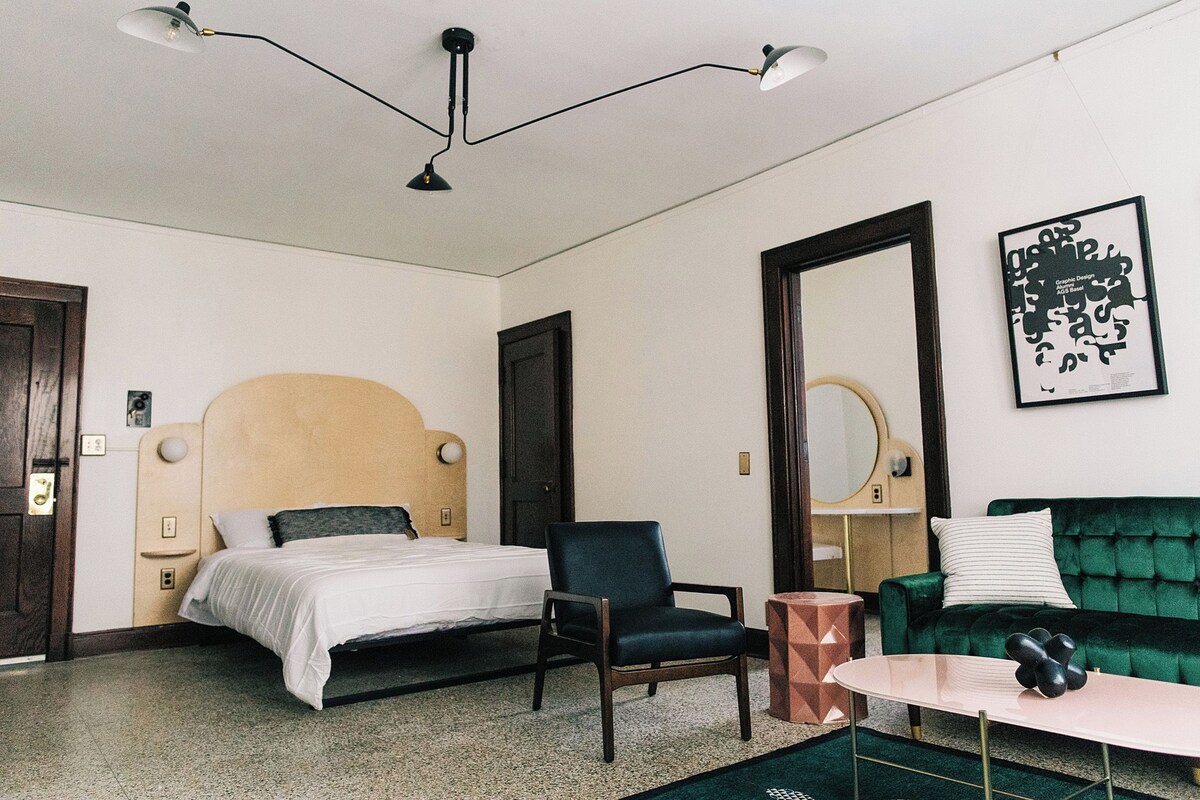 A hotel room with a bed, a chair, a sofa, a small table, and a mirror.
