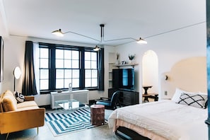 A modern hotel room with a bed, a desk, a chair, a TV, and a large window. - The Wilson by Voyageur Stays (Madison)