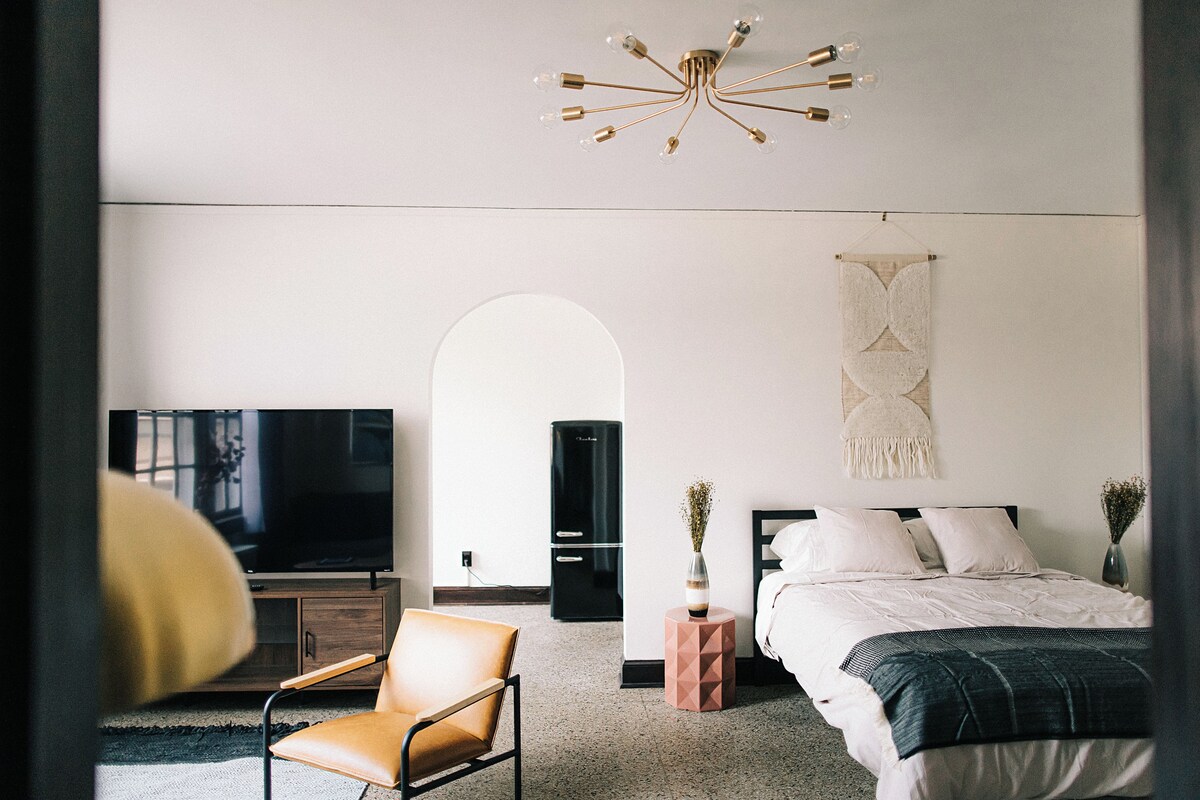 A modern bedroom with a bed, a chair, a TV, and a unique ceiling light fixture.