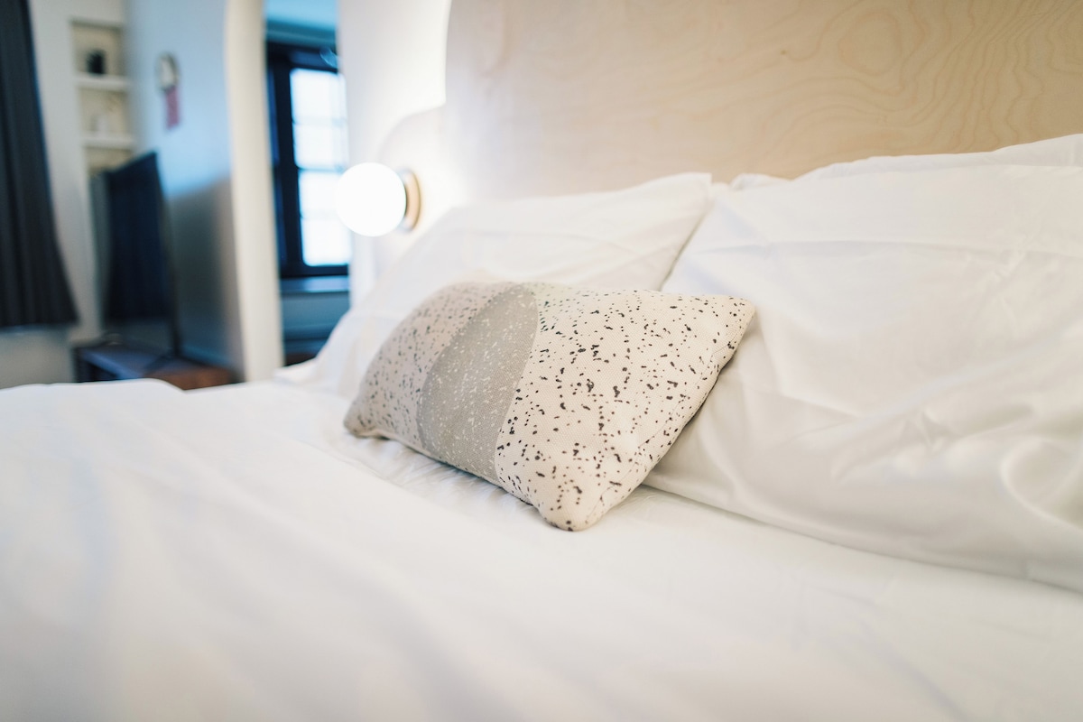 A neatly made bed with white linens and a single decorative pillow.