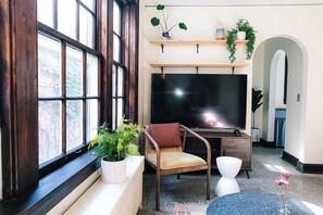 A living room with a large window, a flat-screen TV, a wooden chair, a small table, and a potted plant. - The Wilson by Voyageur Stays (Madison)