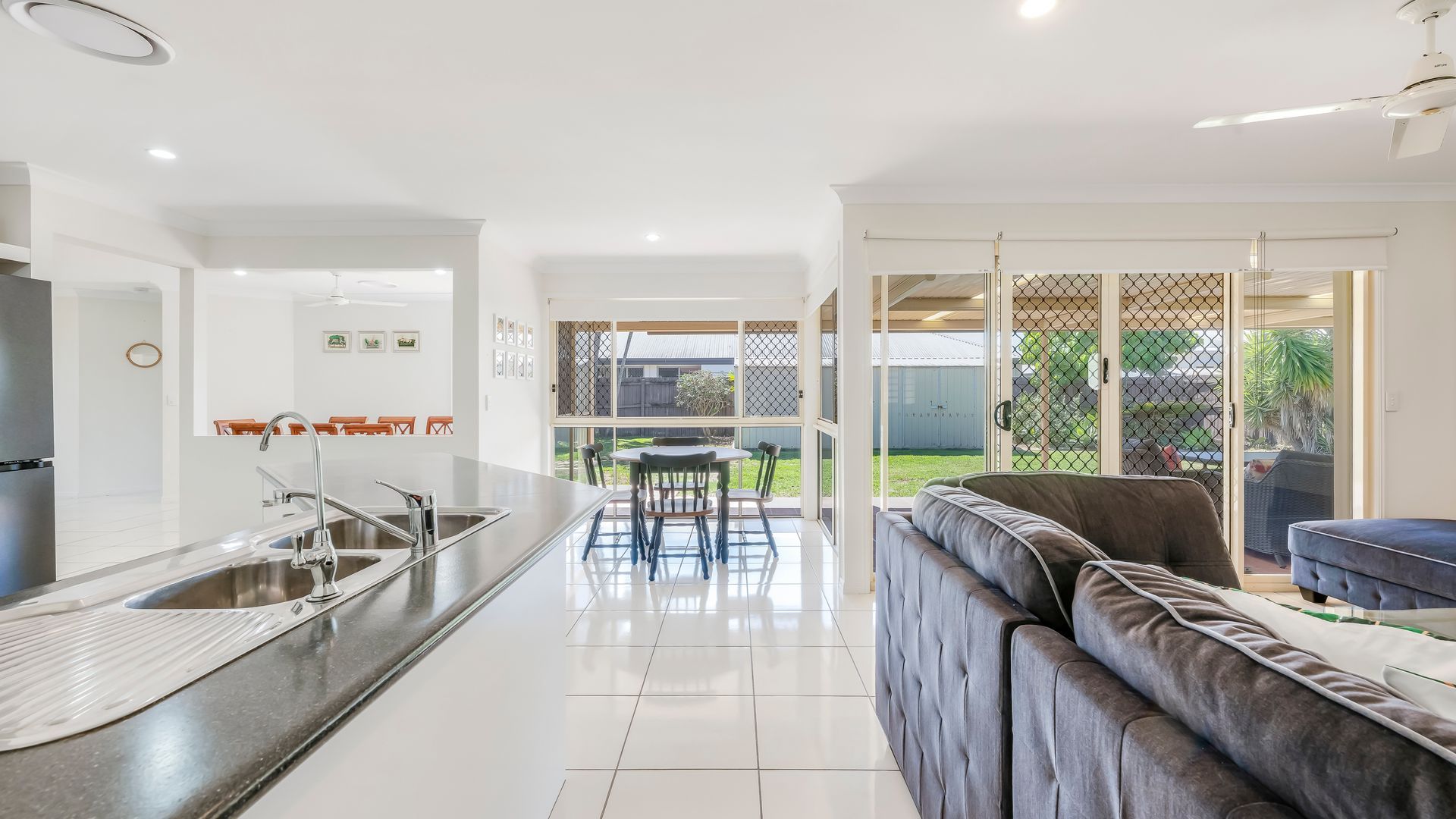 A modern kitchen with a central island, a dining area with chairs, and a living room with a sofa.