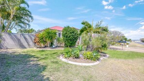 A residential property with a fenced yard, various plants, and a house with a red roof. - 9 Blain Street Bargara (Bargara)