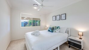 A bedroom with a bed, a nightstand, a lamp, a ceiling fan, and a window with a view of the outside. - 9 Blain Street Bargara (Bargara)