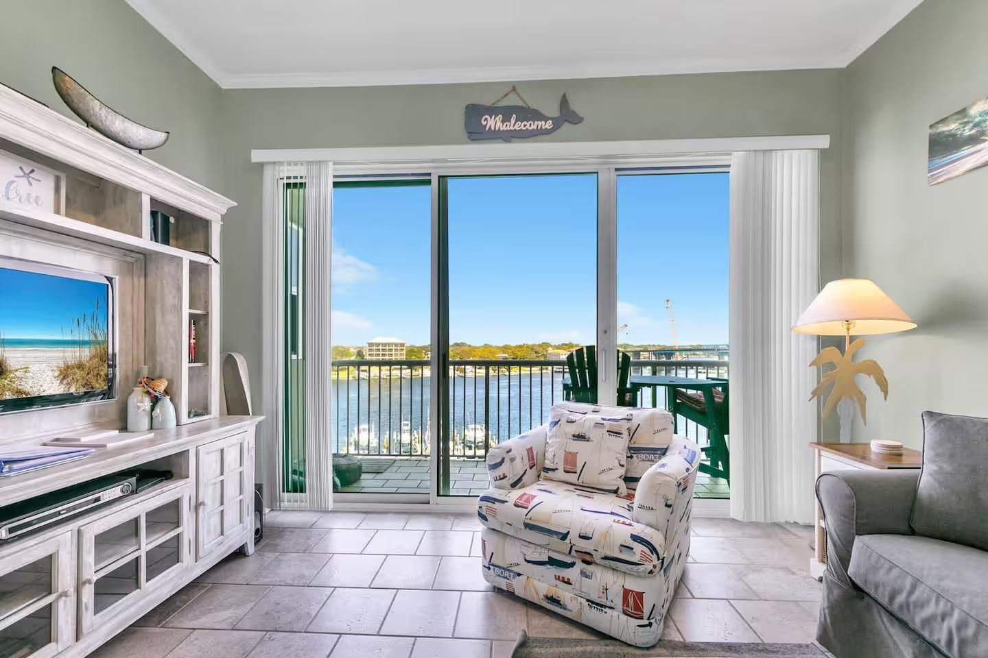 A living room with a view of the water, a sofa, a TV, and a sign that says 'Welcome'.
