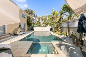 A rectangular swimming pool with a tiled deck, surrounded by palm trees and a covered seating area. - Cozy 1-bedroom Apartment Suite+ Pool & Hot Tub (Key West)