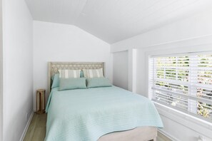A bedroom with a bed, a bedside table, and a window with blinds. - Cozy 1-bedroom Apartment Suite+ Pool & Hot Tub (Key West)