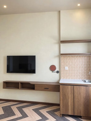A modern kitchen with a flat-screen TV, wooden cabinetry, a tiled backsplash, and a herringbone-patterned floor. - The Mango Stay Thao Dien (An Khanh)