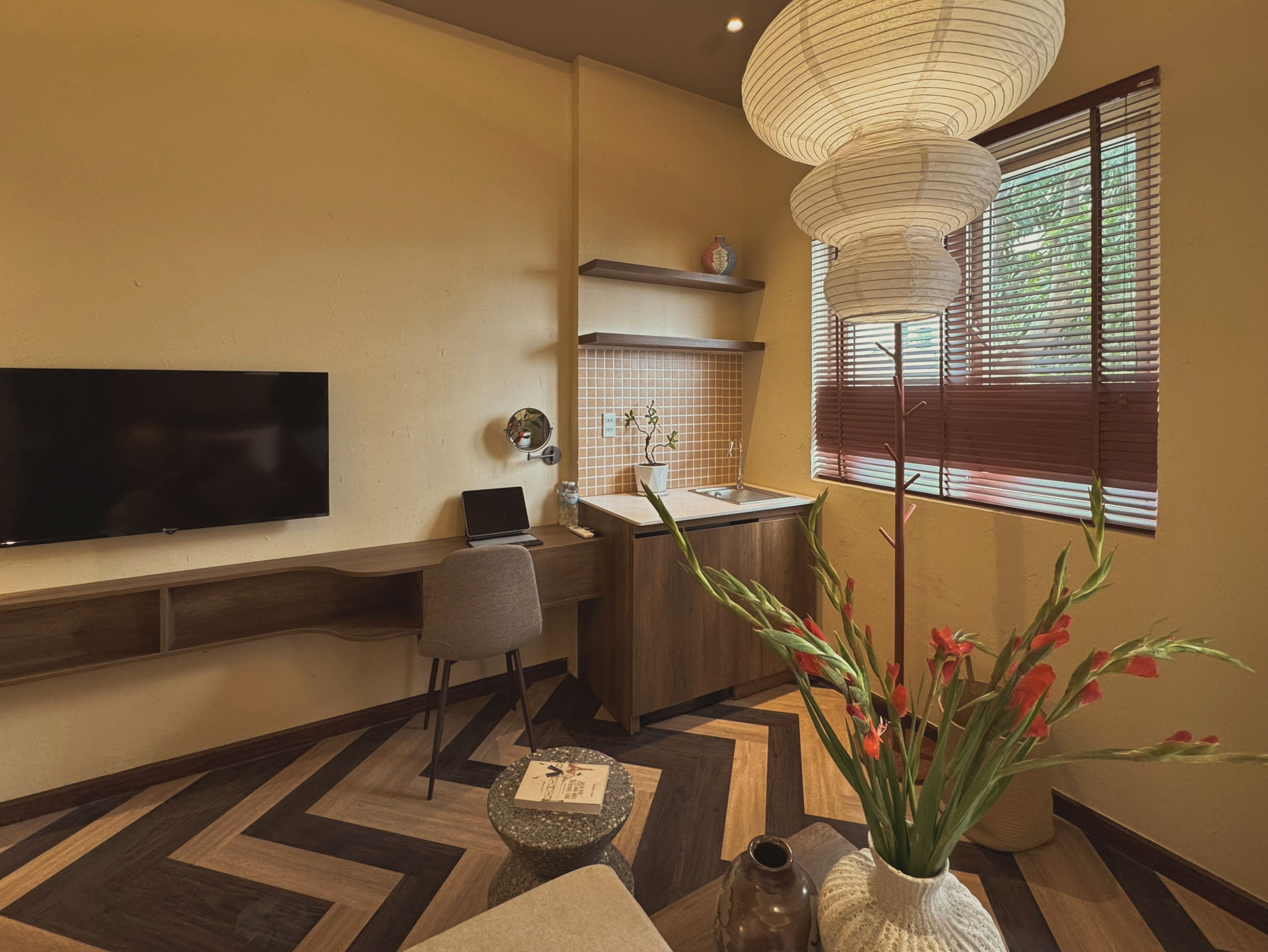 Una sala de estar moderna con un televisor de pantalla plana, una mesita con un libro, un jarrón decorativo y una ventana con persianas.