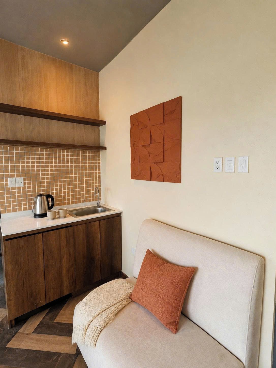 Un espace de vie compact comprenant un coin cuisine, un canapé agrémenté d’un plaid et un élément décoratif mural.
