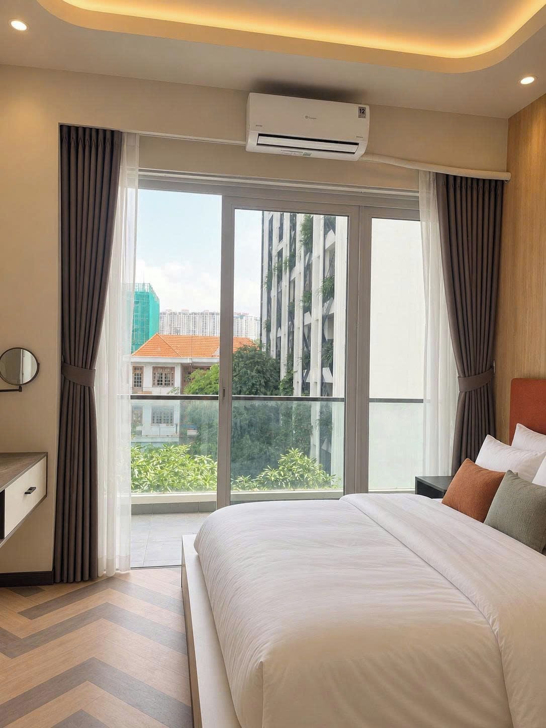 Habitación de hotel con cama, aire acondicionado, ventana con cortinas y vistas a edificios.