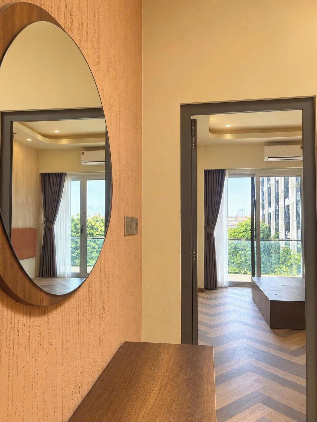 Habitación de hotel con un espejo grande, una tocador de madera, una puerta corrediza de vidrio que da a un balcón y un piso con estampado de espiga.