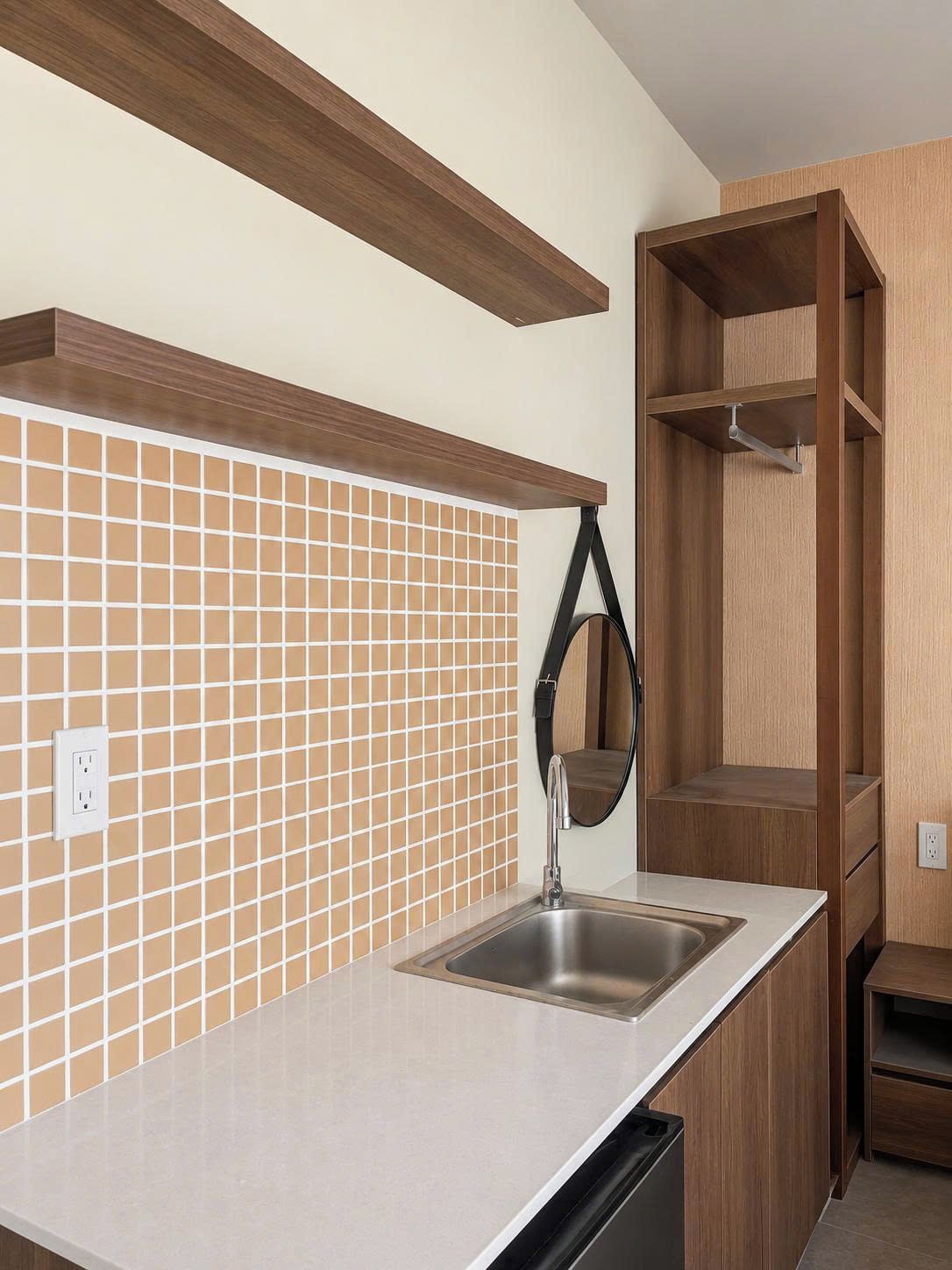 Una cocina con salpicadero de azulejos, un lavamanos de acero inoxidable, armarios de madera y un colgador negro.