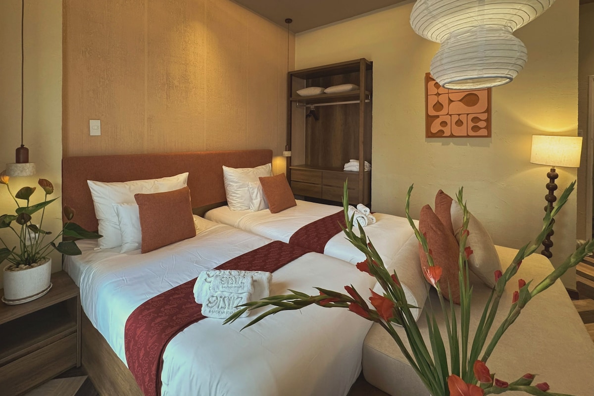 A hotel room with a large bed, a wooden wardrobe, a hanging light fixture, and a wall-mounted artwork.