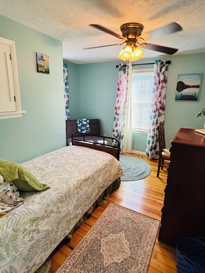 A bedroom with a bed, a desk, a chair, a ceiling fan, and a window with curtains.