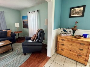 A living room with a sofa, a leather chair, a wooden dresser, and a painting on the wall.