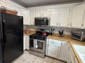 A kitchen with white cabinets, a black refrigerator, a microwave, a stove, and a toaster oven.