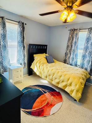 A bedroom with a bed, a nightstand, a ceiling fan, and a window with curtains. - It's a Wonderful House! (Indiana)