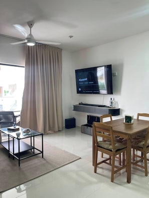 A modern living room with a flat-screen TV, a ceiling fan, a dining table with chairs, and a large window with curtains. - Bayahibe Sunshine 2BR Pool Close to the Beach (San Rafael del Yuma)