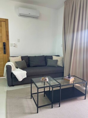 A living room with a grey sofa, a glass coffee table, and a beige curtain. - Bayahibe Sunshine 2BR Pool Close to the Beach (San Rafael del Yuma)