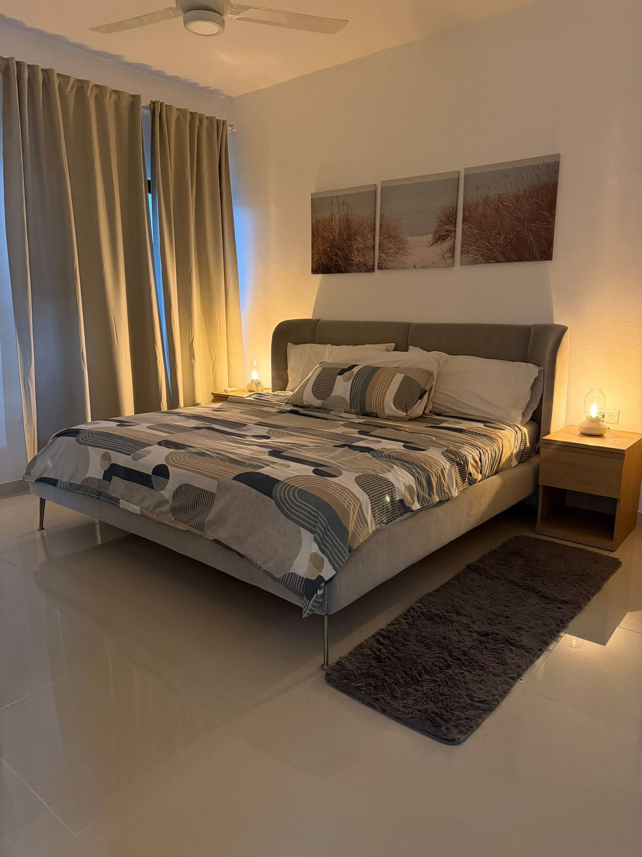 A modern bedroom with a large bed, a nightstand with a lamp, and a ceiling fan.