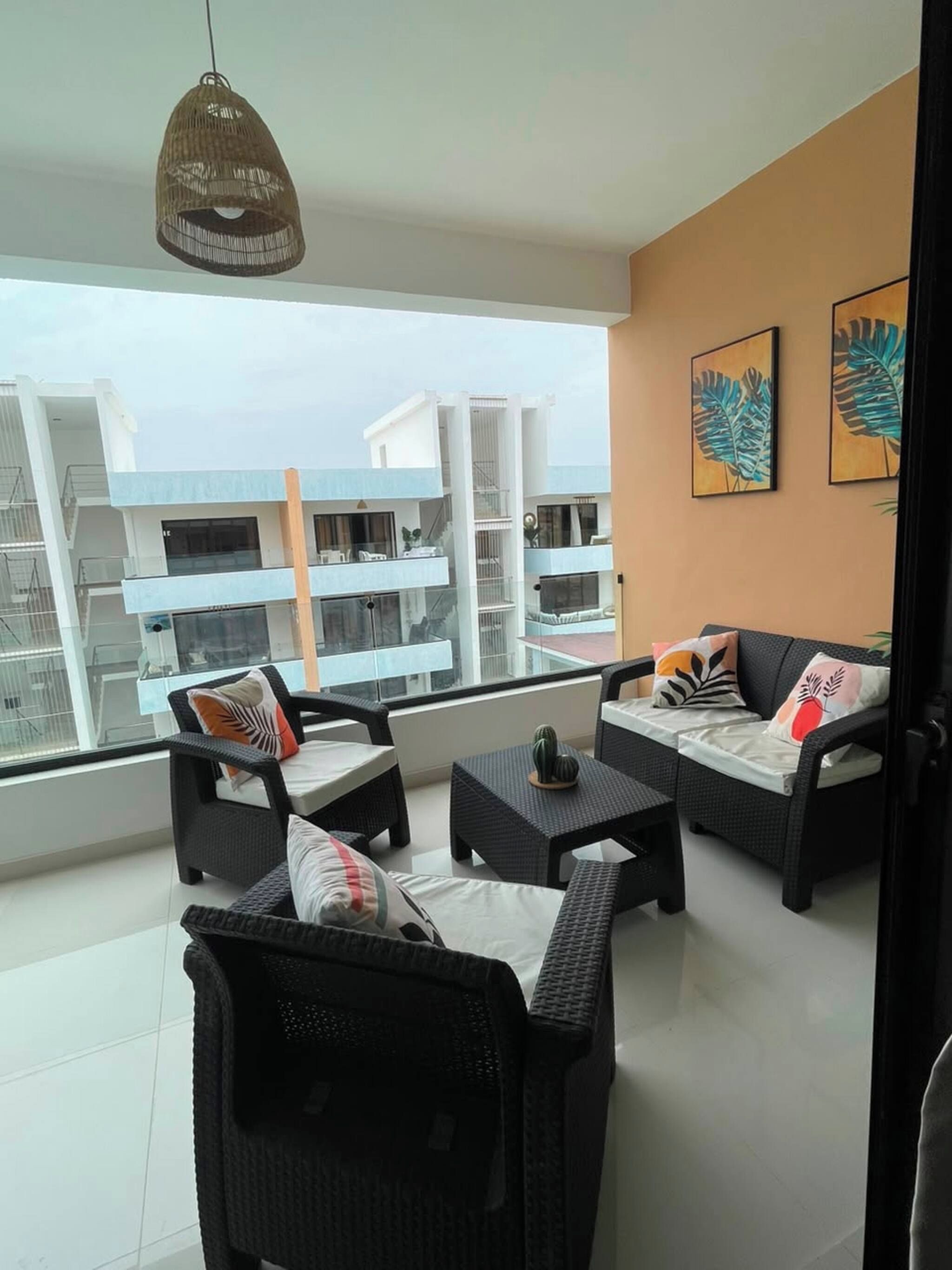 A balcony with wicker furniture, a hanging light fixture, and a view of adjacent buildings.