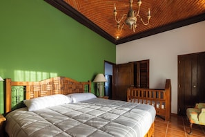 Een slaapkamer met een houten hoofdeinde, een bed met een gewatteerde spreideken, een nachtkastje, een lamp, een kledingkast en een stoel.