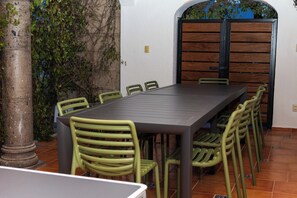 A dining area with a long table and multiple chairs, a pillar, and a wooden door in the background. - Spacious Home for 10 – 2 km from Peña de Bernal (Bernal)