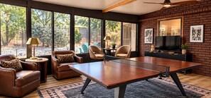 A room with a ping pong table, leather chairs, a television, and large windows. - Canyon & Sage Sedona Retreat (Sedona)