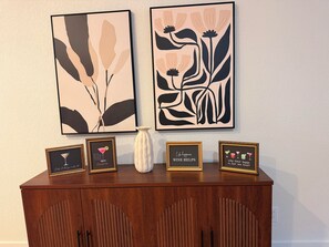 A wooden cabinet with framed items including a martini glass, a quote about wine, and a decorative vase. - Canyon & Sage Sedona Retreat (Sedona)