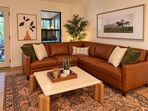 A living room with a brown leather sectional sofa, a wooden coffee table, patterned rugs, and framed artwork on the walls. - Canyon & Sage Sedona Retreat (Sedona)