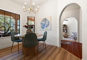 Un coin repas avec une table ronde, deux chaises, un vase de fleurs et un lustre.
