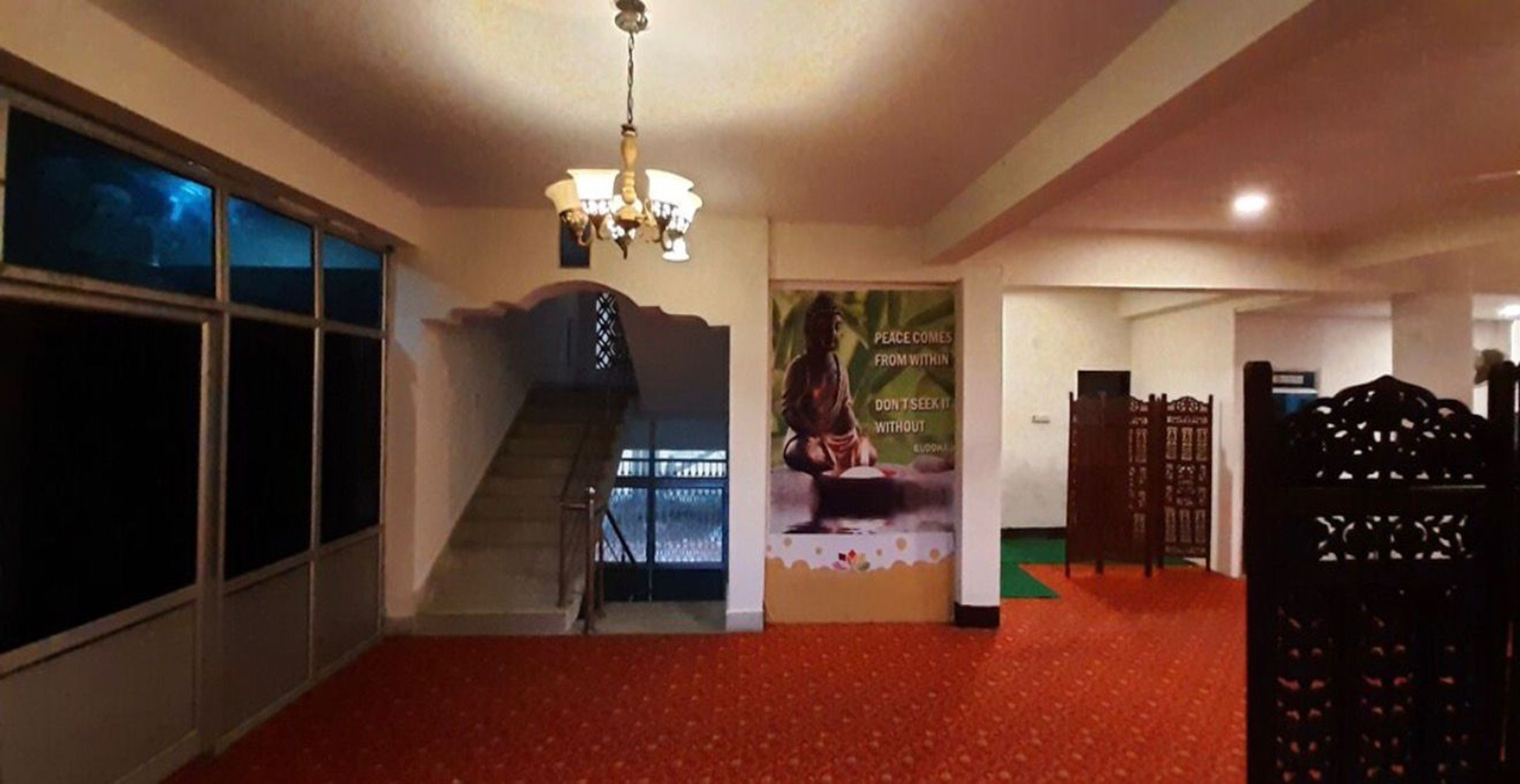 Un couloir d’hôtel avec un tapis rouge, un escalier, un lustre et une affiche représentant une image de Bouddha.