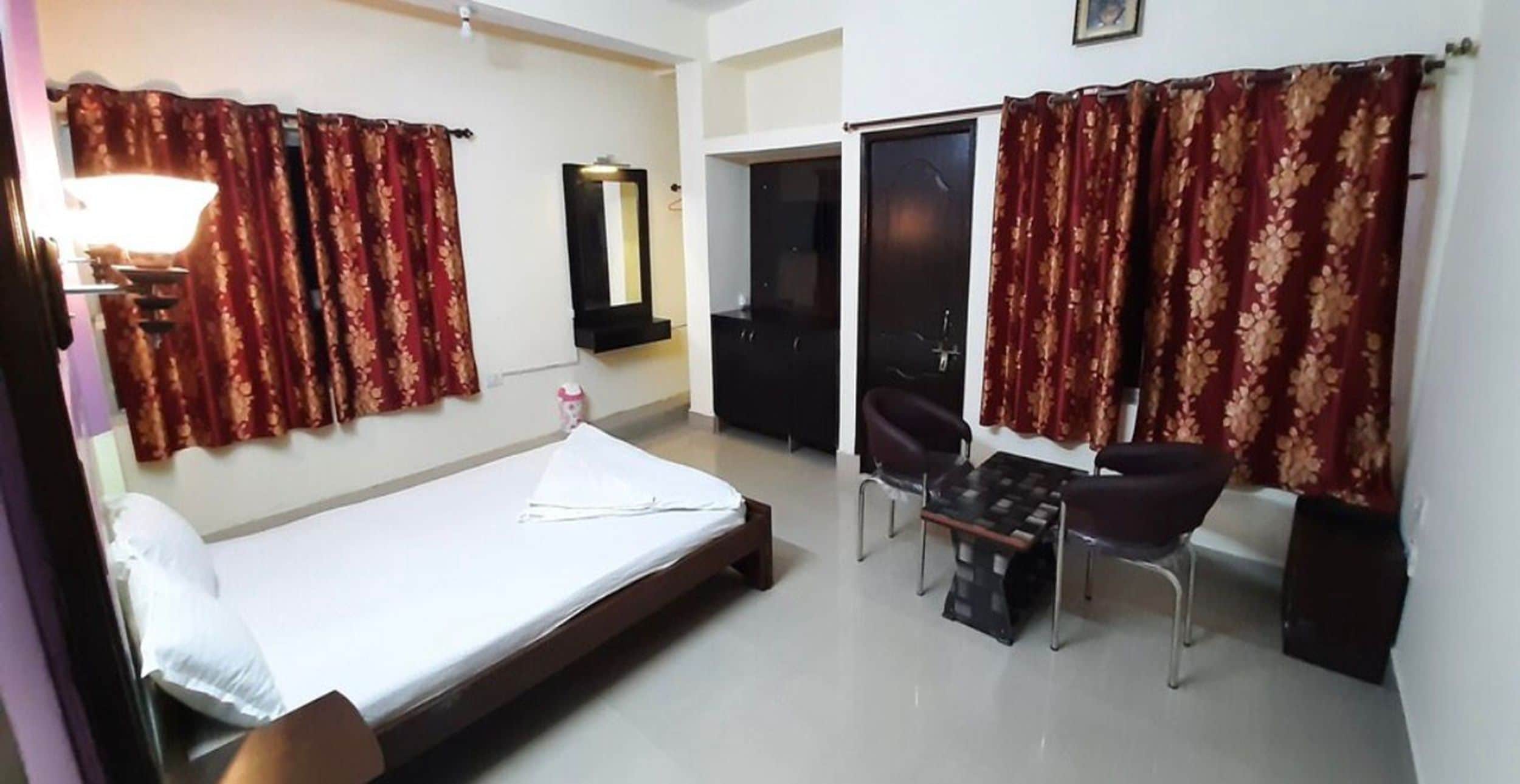 A room with a bed, a desk, two chairs, a lamp, and curtains.