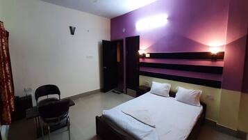 Una habitación de hotel con cama, una silla, un escritorio y una puerta.