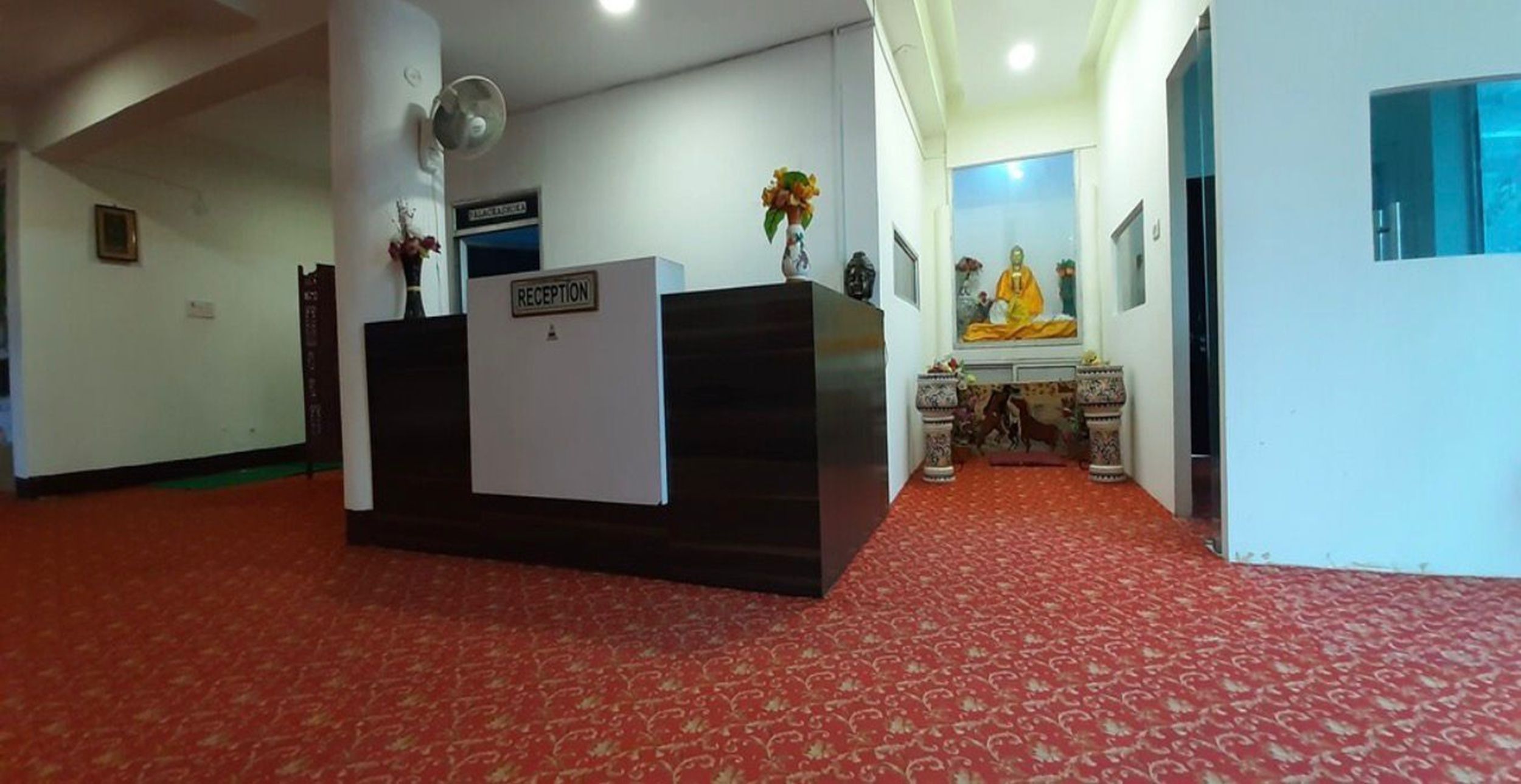 Un espace d’accueil comprenant un comptoir de réception, un ventilateur fixé au mur et une statue de Bouddha.