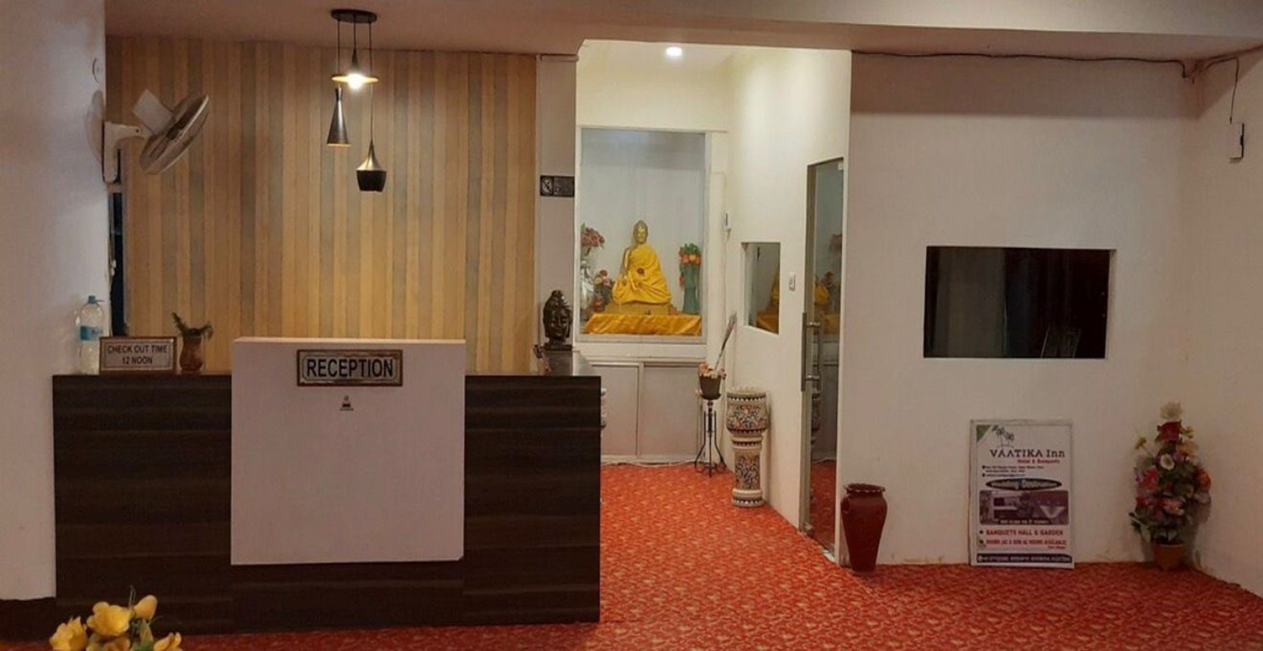 Un área de recepción con mostrador, una estatua de Buda y un cartel de Vaatika Inn.
