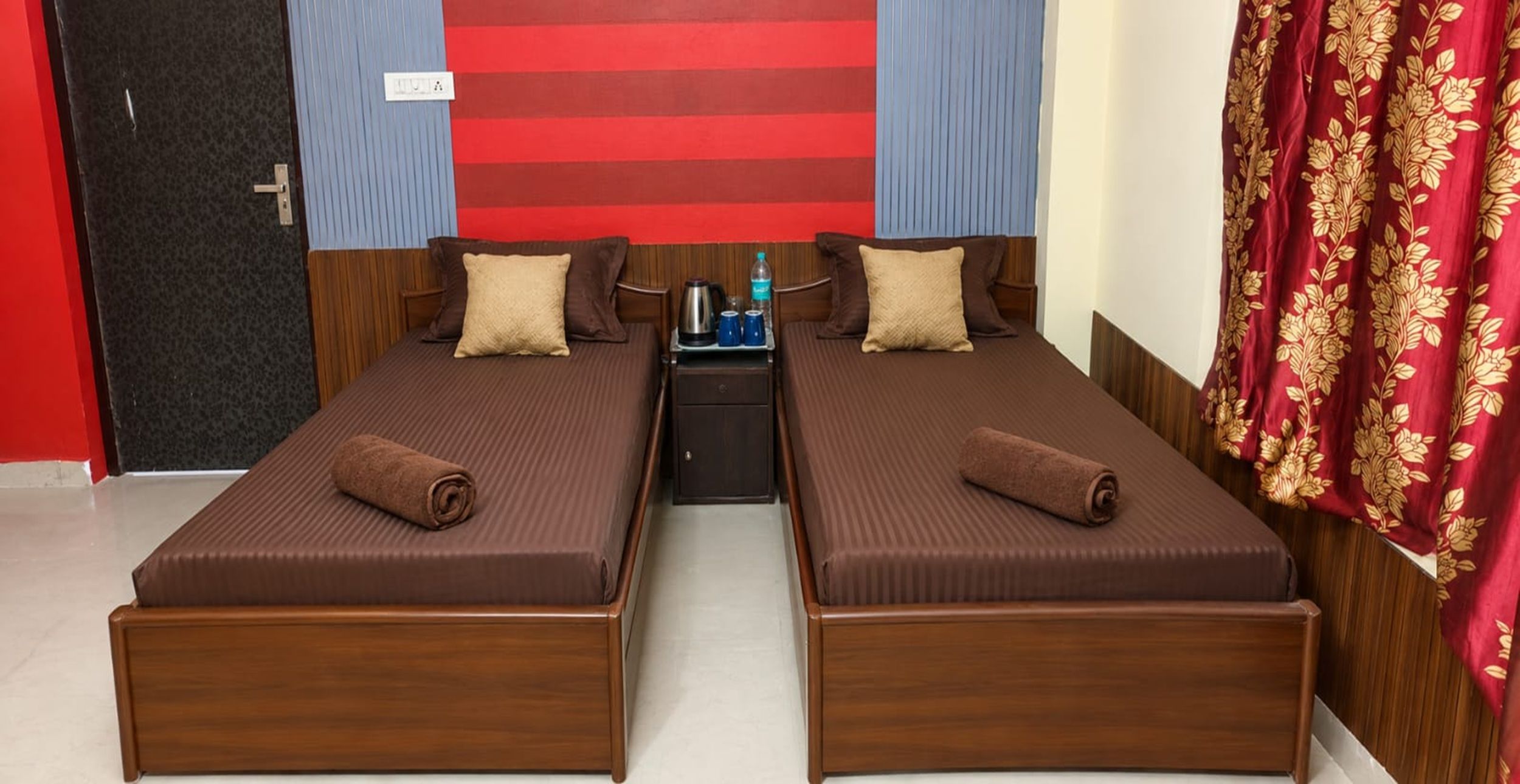 Habitación doble con dos camas, una mesita de noche y pared con rayas azules y rojas.