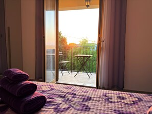 Ein Zimmer mit Bett, einem Balkon mit Tisch und Stühlen sowie Blick ins Freie.