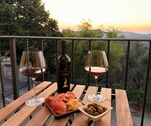 Ein Holztisch mit zwei Weingläsern, einer Weinflasche und einem Teller mit Essen auf einem Balkon.