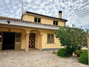 Um edifício de dois andares com telhado de cerâmica, entrada em tijolo e um pequeno jardim com vasos de plantas.